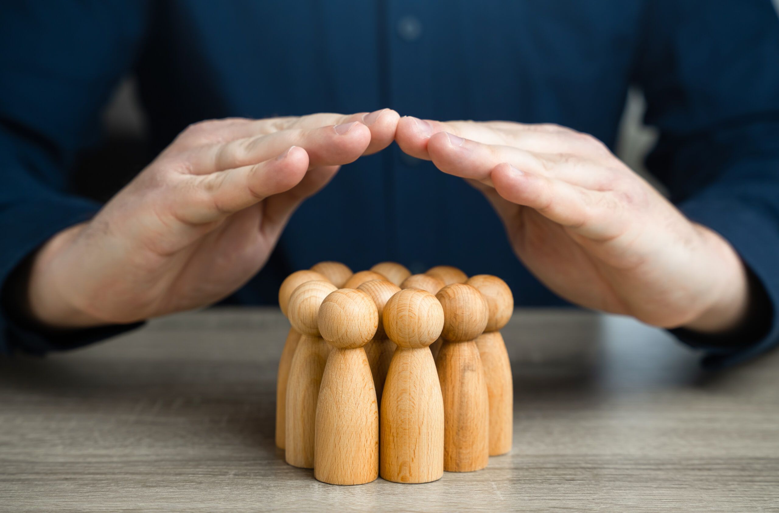 A man covers a group of people figures with house roof gesture. The concept of insurance and social protection. Life insurance. Customer care. Human resources.